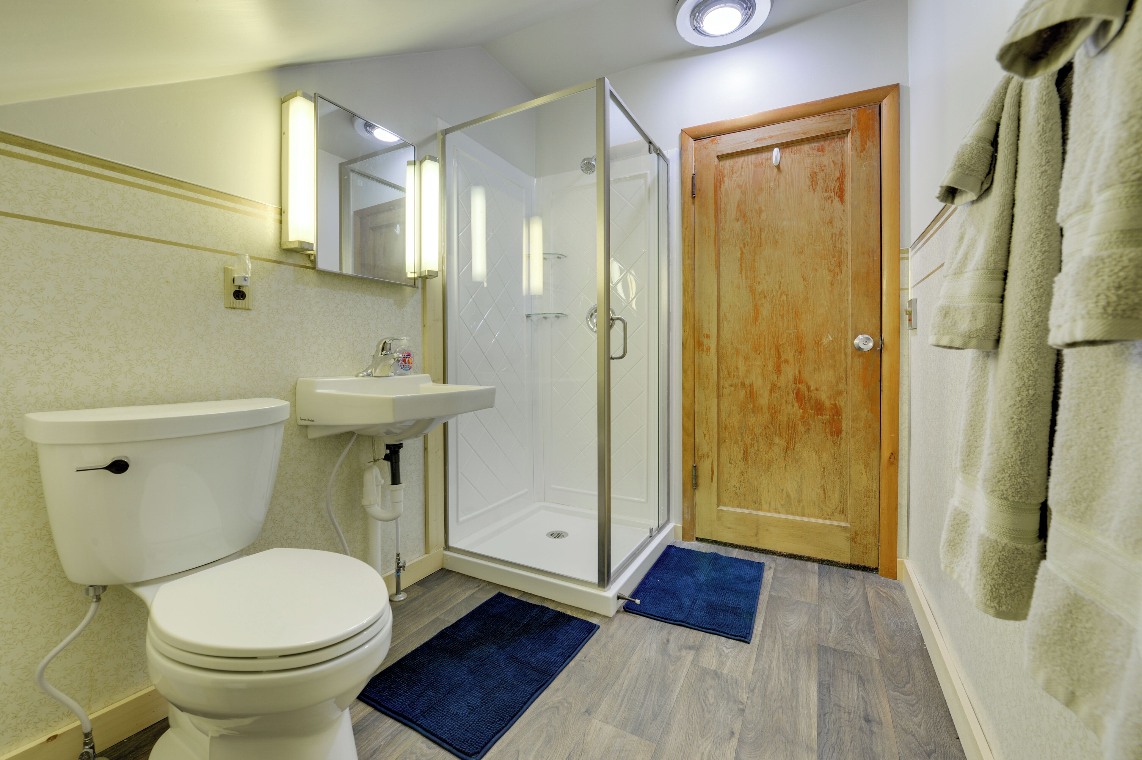 Ein Badezimmer mit Toilette, Waschbecken, Dusche und Holztür.