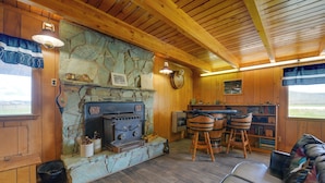 L’intérieur d’un chalet rustique, avec une cheminée en pierre, des murs en bois, un coin repas doté d’un bar et un canapé.