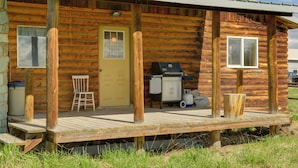 Une cabane en rondins avec une véranda, une porte, une fenêtre, un barbecue et une chaise.