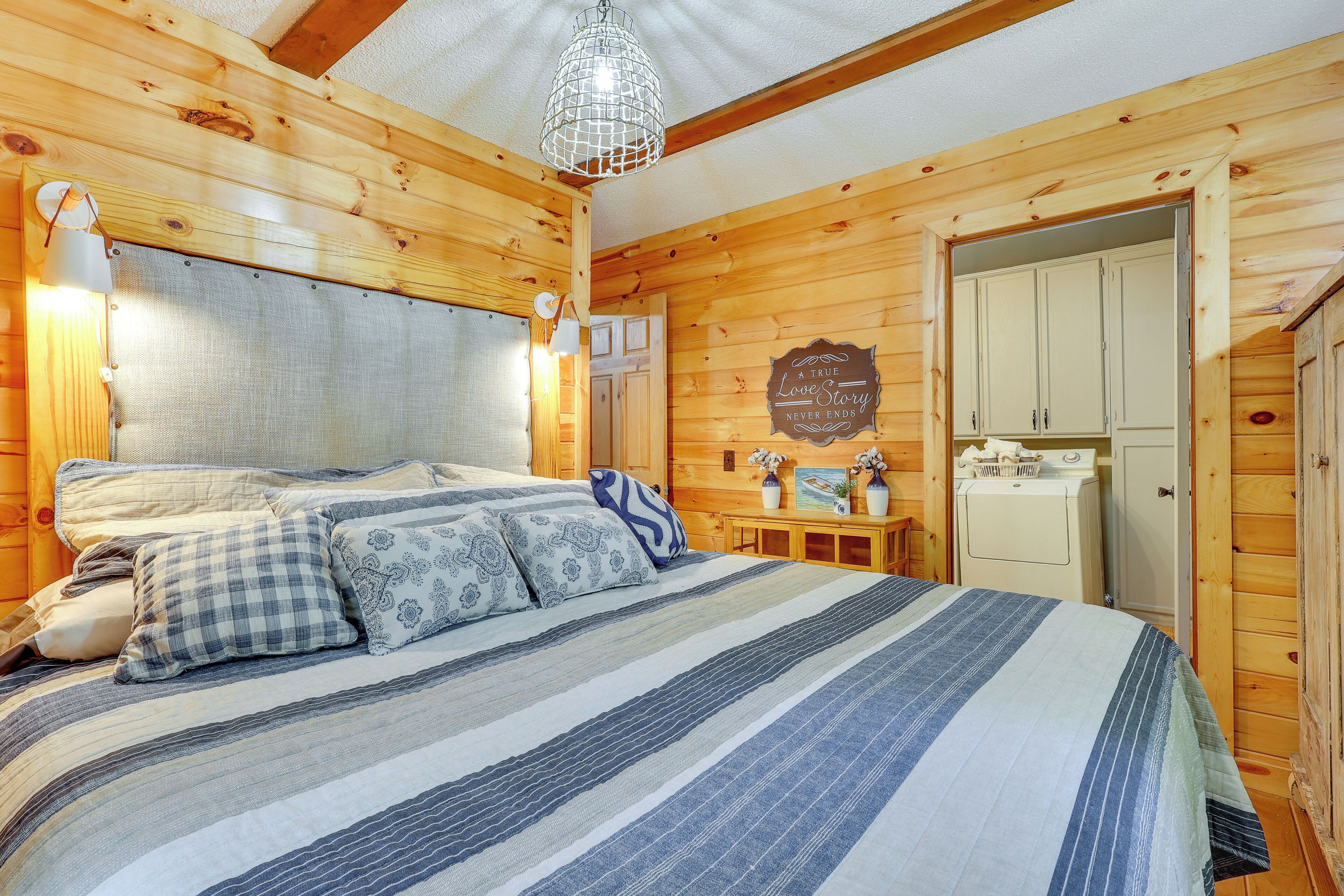 A wooden cabin bedroom with a bed, a nightstand, a dresser, and a small table with decorative items.