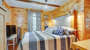 Ein Schlafzimmer einer Holzhütte mit einem Bett, einem Schreibtisch, einem Fernseher und einer Pendelleuchte.