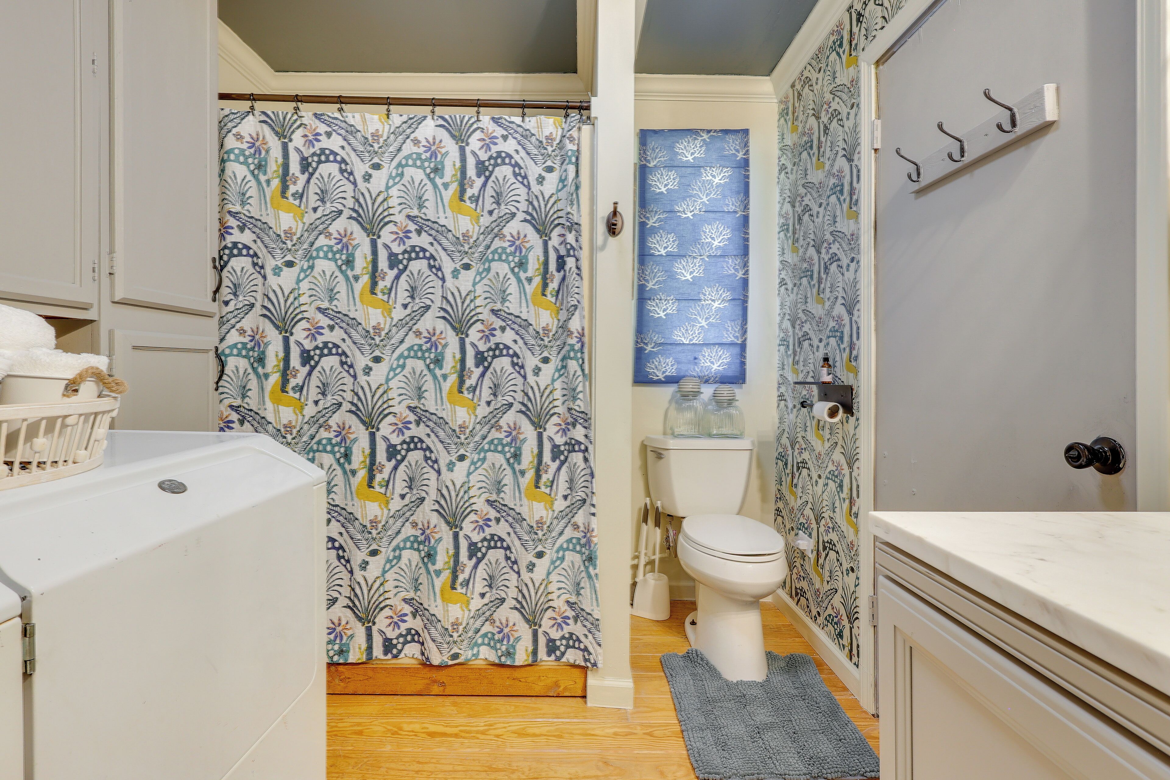 A bathroom with a shower curtain featuring a floral pattern, a toilet, a sink with a mirror, and a towel rack.