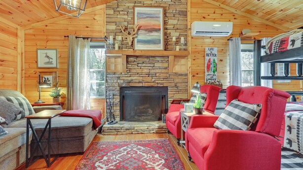 Ein gemütliches Blockhaus mit Kamin aus Stein, Holzwänden, einem roten Sofa und einem gemusterten Teppich.