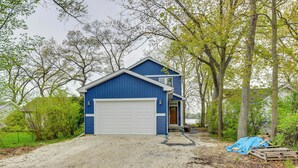 A two-story blue house with a white garage door, surrounded by trees and a gravel driveway. - Lakefront Burlington Vacation Rental: Dock + Beach (Burlington)