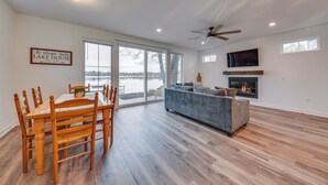 A spacious living room with a fireplace, a dining area with wooden chairs, and large windows overlooking a body of water. - Lakefront Burlington Vacation Rental: Dock + Beach (Burlington)