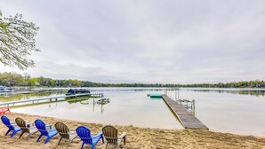 A lakeside beach with blue and brown chairs, a wooden dock, and a calm water body. - Lakefront Burlington Vacation Rental: Dock + Beach (Burlington)