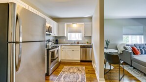 A modern kitchen with stainless steel appliances, white cabinetry, and a dining area with a gray sofa and a coffee table. - Wyandotte Vacation Rental Apartment Near Hospital! (Wyandotte)