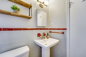 Bathroom features a pedestal sink, mirror, and potted plant, with a toilet and towel rack nearby.