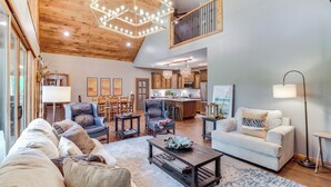 A spacious living room with a high ceiling, wooden beams, a dining area, and a kitchen in the background. - Gorgeous Drasco Home Near Greers Ferry Lake! (Drasco)