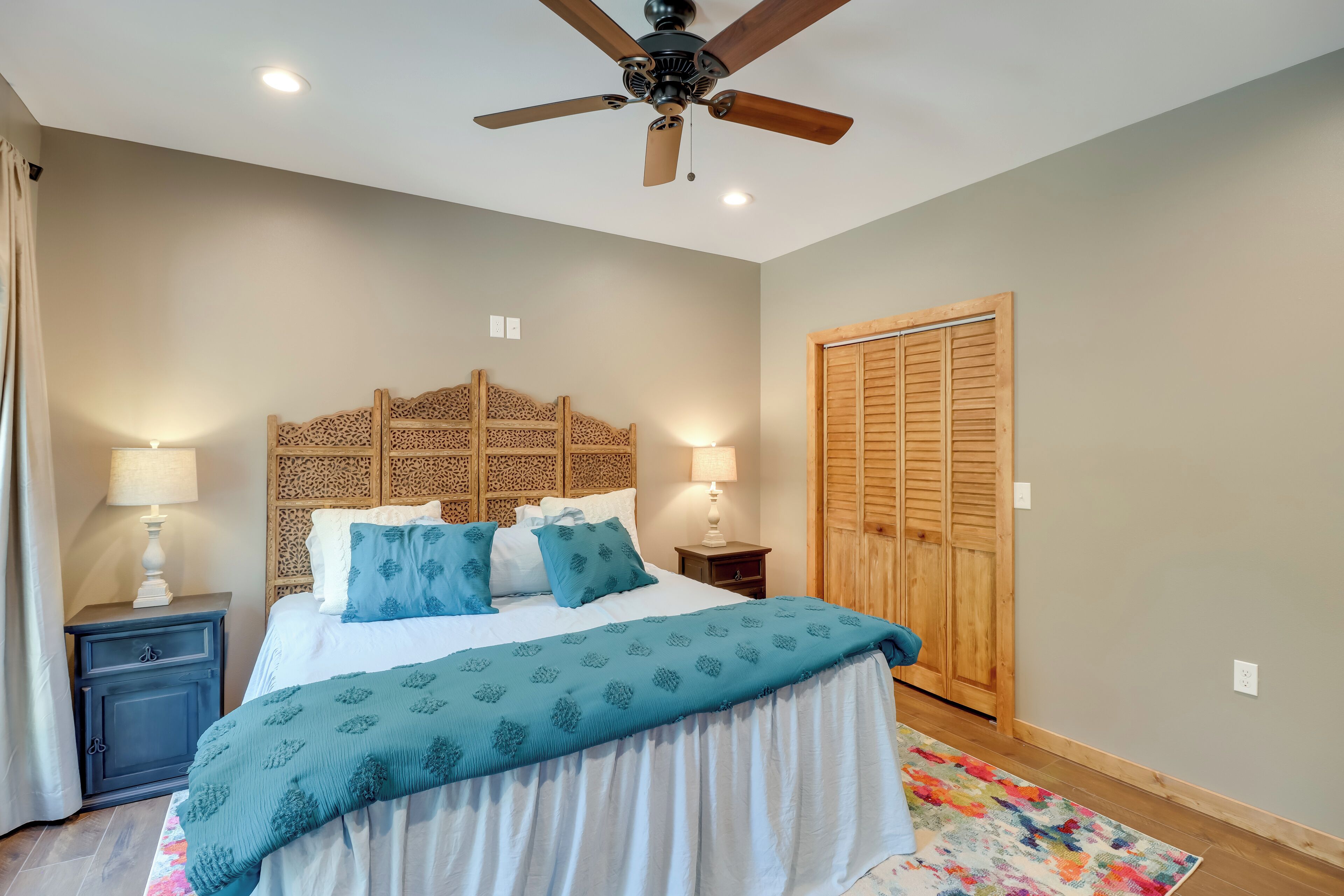 A bedroom with a bed, nightstands, a ceiling fan, a wooden headboard, and a wardrobe.