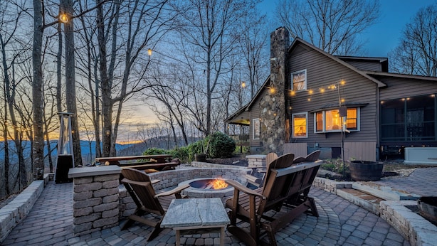 A patio with a fire pit, stone seating, and a view of a house with string lights. - Near Highlands: 36-acre Scaly Mountain Lodge (Scaly Mountain)