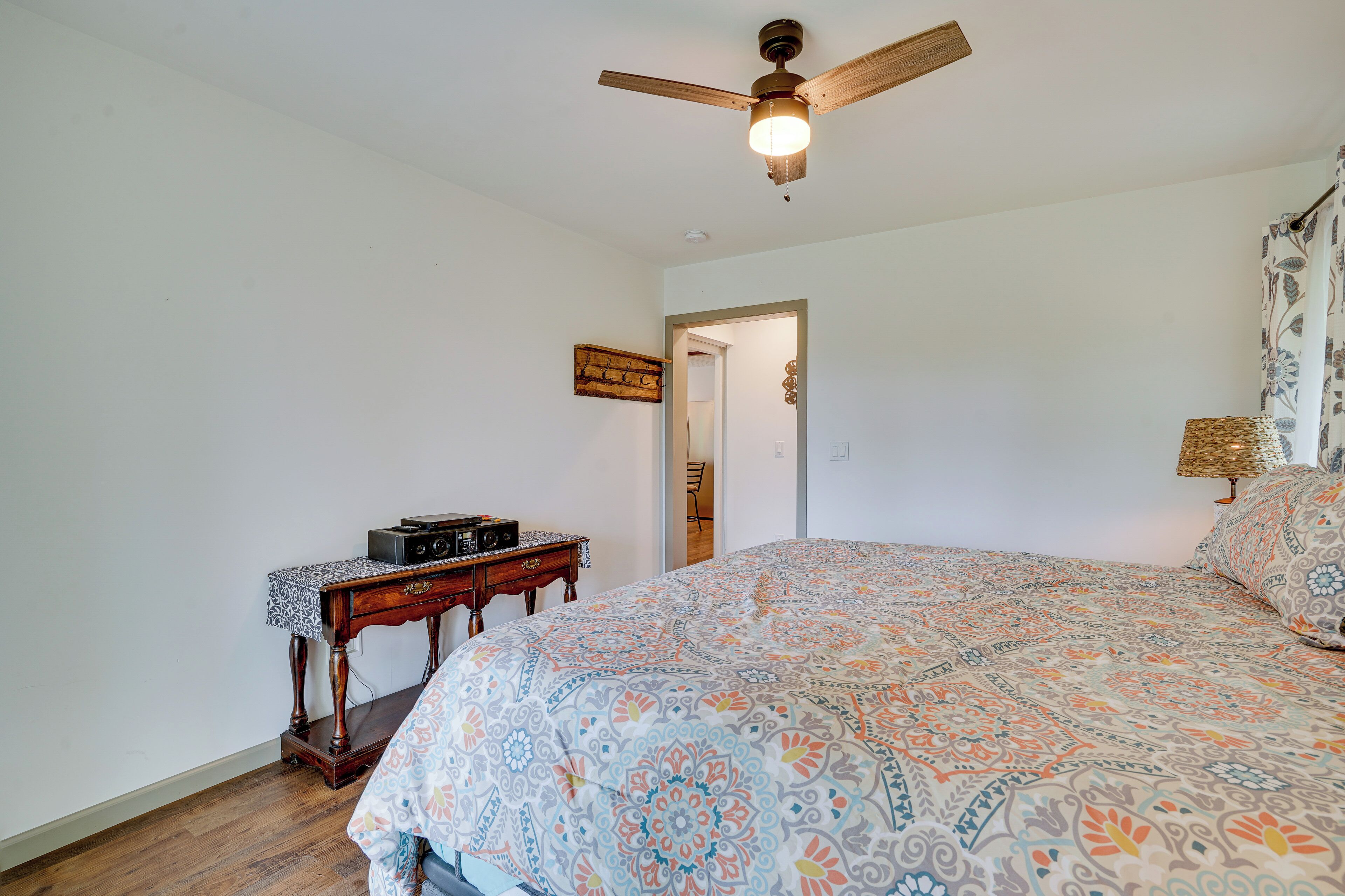 A bedroom with a bed, a ceiling fan, a wooden nightstand, and a door leading to another room.