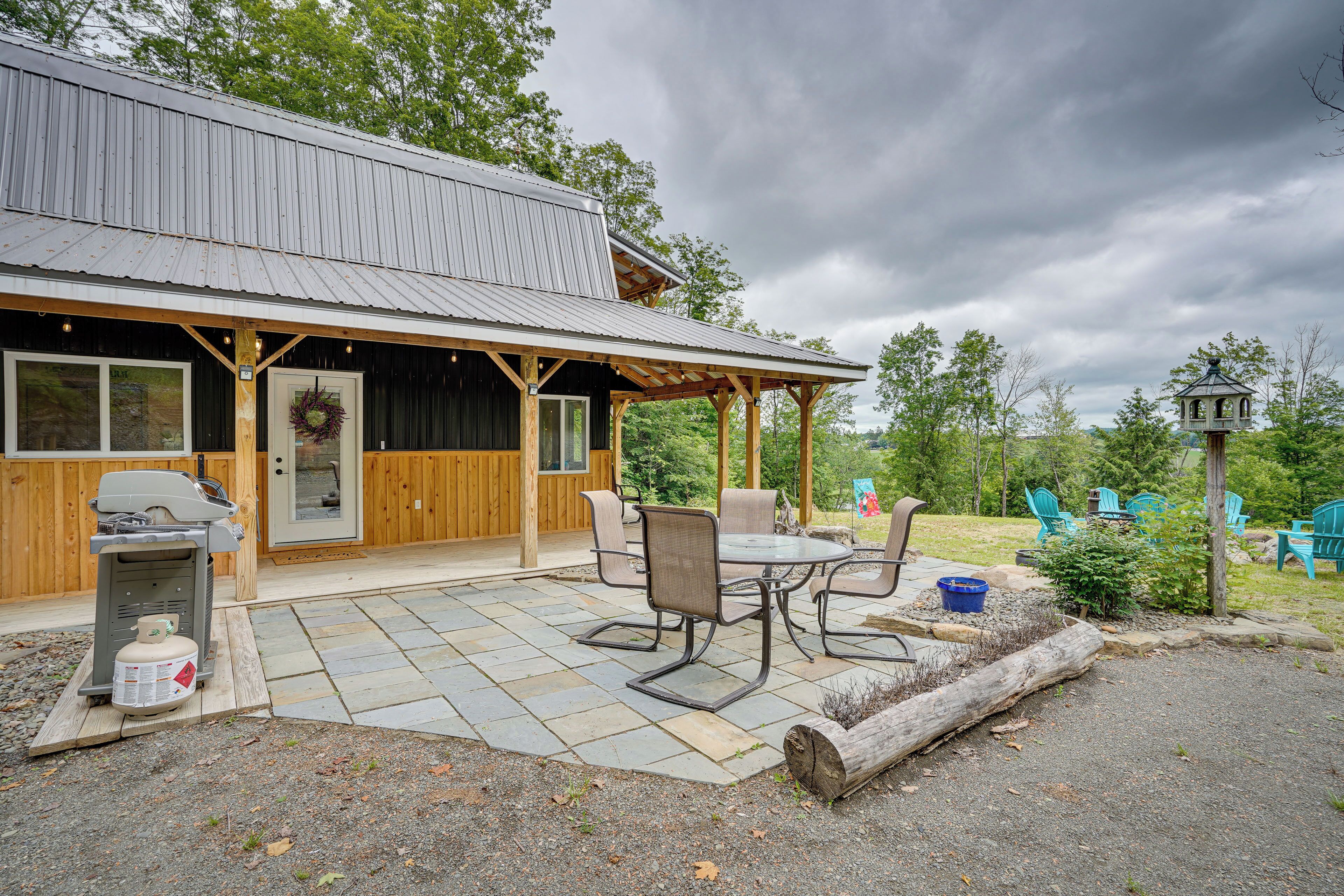 A rustic cabin with a covered patio, outdoor seating, and a grill.