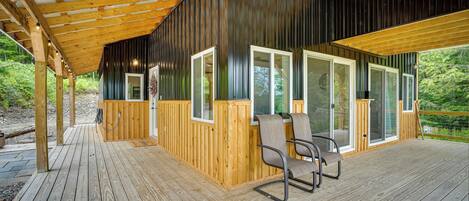 A wooden deck with a covered area, large windows, and a chair.