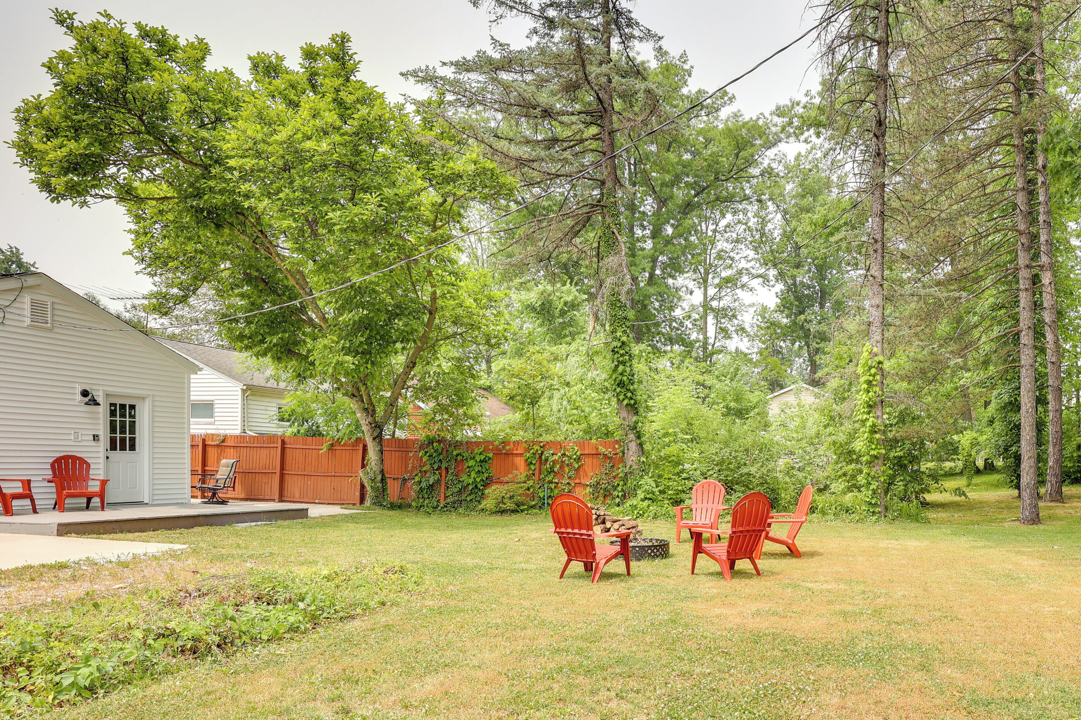 Un jardin avec une terrasse en bois, un foyer et des fauteuils Adirondack rouges.