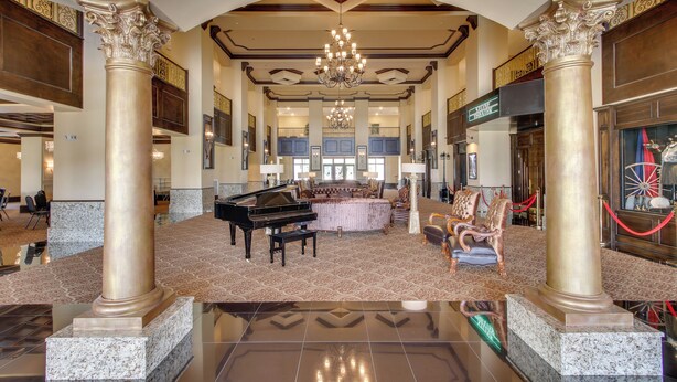 Un vestíbulo imponente con un piano de cola, columnas ornamentales, una araña de cristal y una zona de estar amplia.