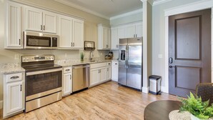 Una cocina con armarios blancos, electrodomésticos de acero inoxidable y piso de madera.