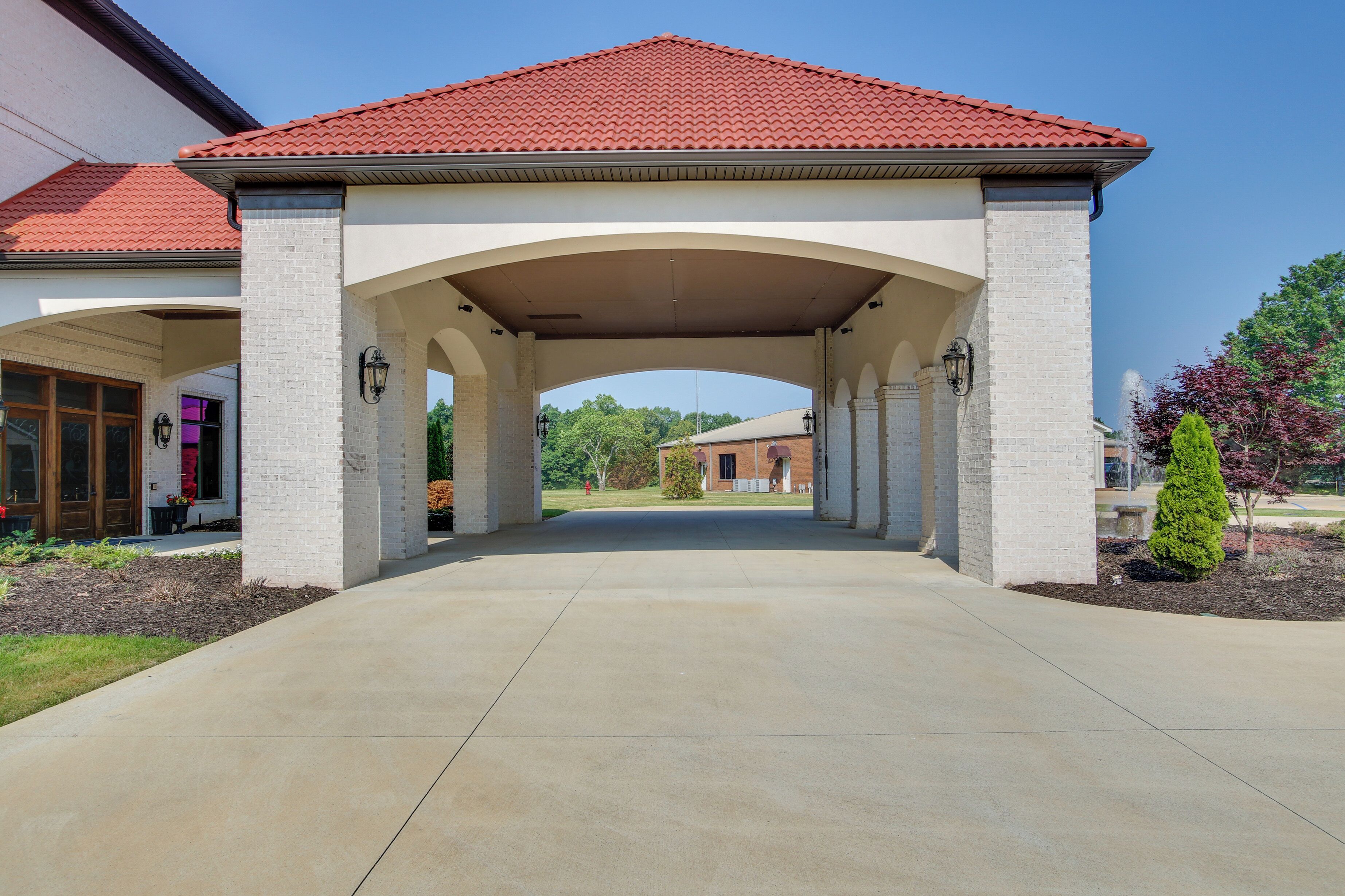 A covered driveway leading to a building with a red-tiled roof and white brick columns.