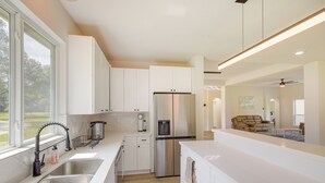 Una cocina moderna con armarios blancos, electrodomésticos de acero inoxidable y un amplio ventanal con vistas al exterior.