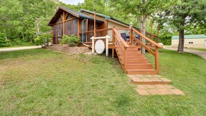 Uma cabana de madeira com uma escadaria que dá para um deck, rodeada por árvores e um gramado.