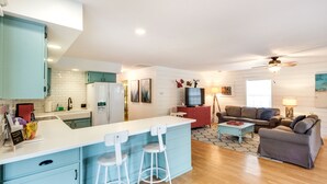 Cozinha moderna com ilha central, sala de jantar com mesa vermelha e sala de estar com sofá e televisão.