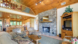 A spacious living room with a stone fireplace, wooden furniture, and a balcony. - Almond Vacation Rental w/ Mountain Views! (Almond)
