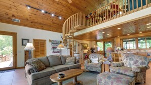 A spacious living area with a wooden ceiling, a sofa, a coffee table, and a patterned armchair. - Almond Vacation Rental w/ Mountain Views! (Almond)