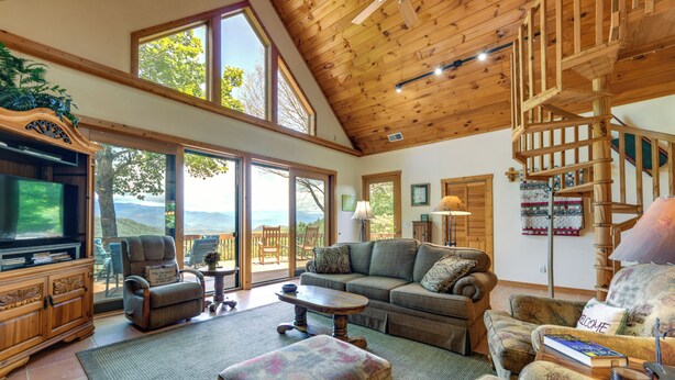 A spacious living room with a wooden ceiling, large windows, a fireplace, and a cozy seating area. - Almond Vacation Rental w/ Mountain Views! (Almond)
