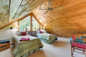 Ein gemütliches Schlafzimmer unter dem Dach mit zwei Betten, einem Deckenventilator und einem großen Fenster, das für natürliches Licht sorgt.