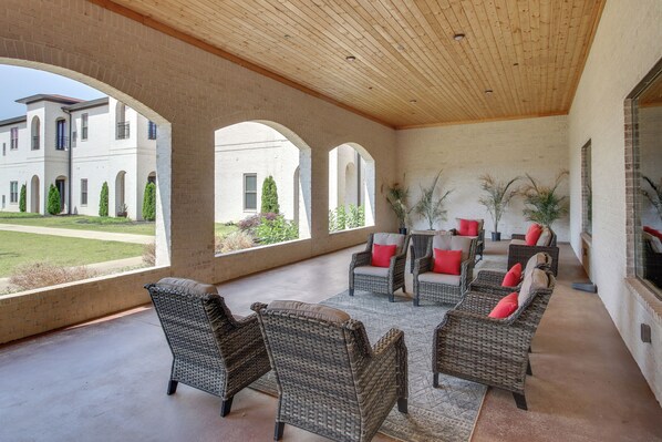 A covered patio with wicker furniture and red cushions, large windows, and a view of a building and lawn. - Resort Apartment in Loretto w/ Private Patio! (Loretto)