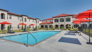 A swimming pool with lounge chairs and red umbrellas, surrounded by a building with arched windows and a red roof. - Loretto Vacation Rental w/ Community Resort Perks (Loretto)