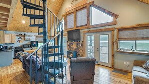 A spacious living area with a wooden staircase, a fireplace, and a large window overlooking a body of water.