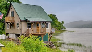 Una casa con techo verde, terraza de madera y vista al lago.