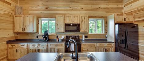 A modern kitchen with wooden cabinetry, a stainless steel sink, a microwave, a stove, and a refrigerator.