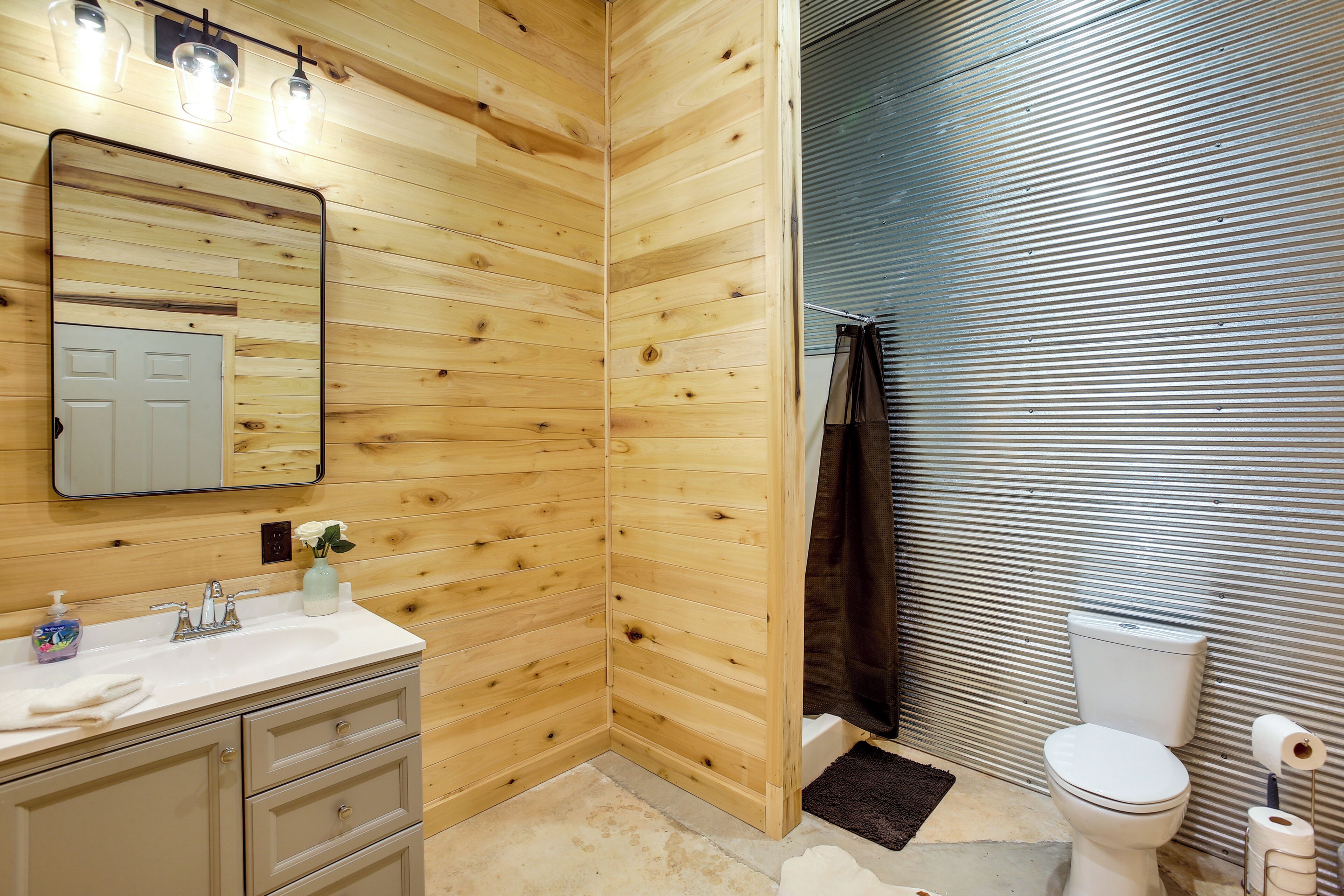 A bathroom with wooden walls, a white sink with a mirror, and a toilet.