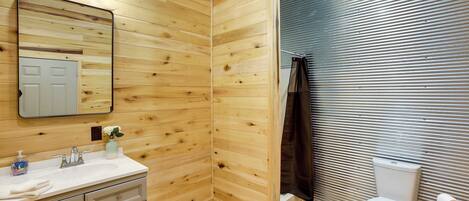 A bathroom with wooden walls, a white sink with a mirror, and a toilet.