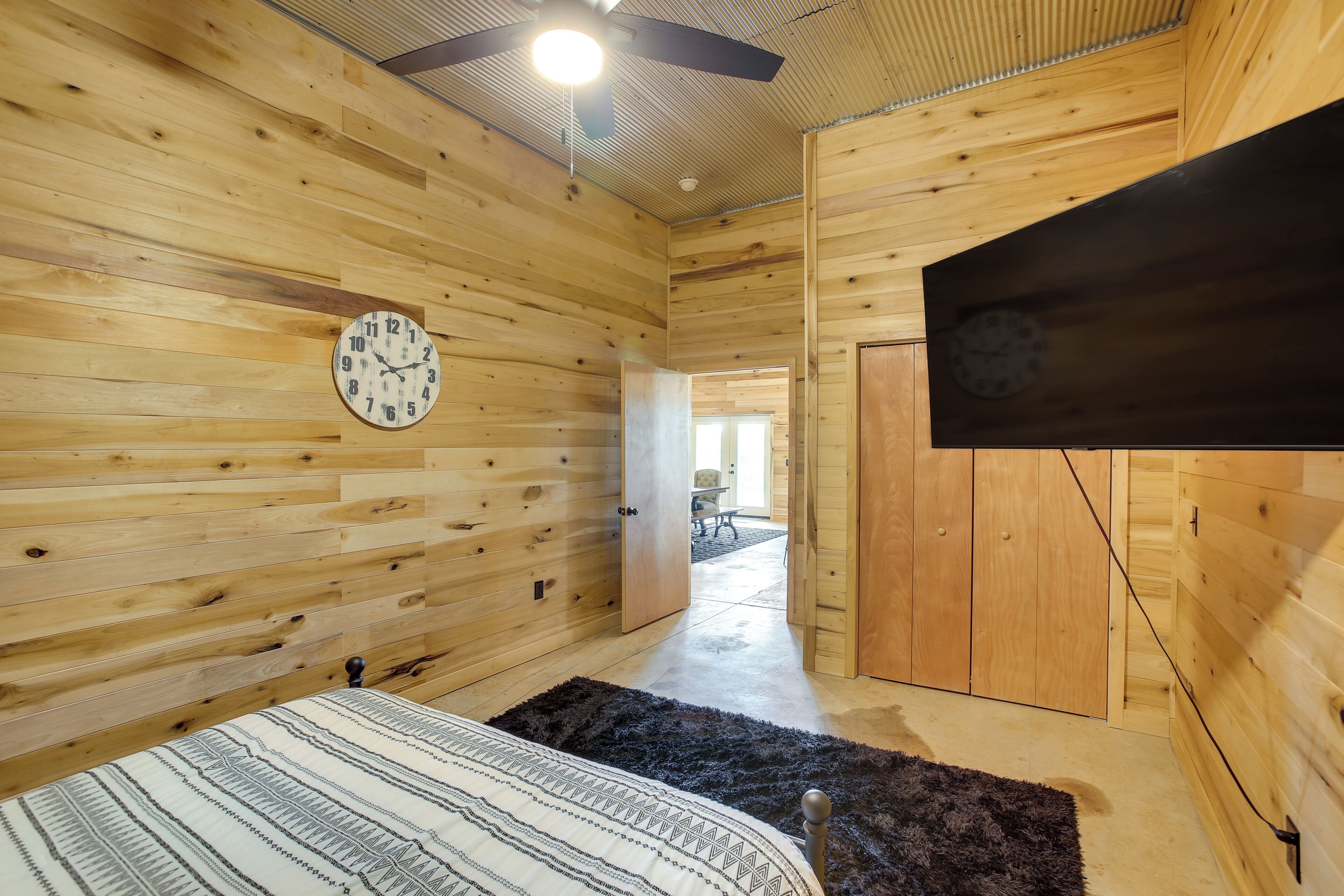 A wooden-paneled room with a bed, a clock, and a ceiling fan.