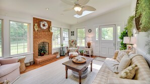 A spacious living room with a fireplace, a ceiling fan, and a large window overlooking a garden. - Mobjack Bay Rental on Private Cove! (Bohannon)