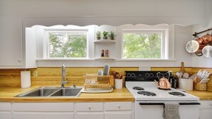 A kitchen with a wooden countertop, white cabinets, a stainless steel sink, a stove, and a window with a view of trees. - Mobjack Bay Rental on Private Cove! (Bohannon)