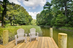A wooden deck with two Adirondack chairs facing a river, surrounded by lush greenery and trees. - Mobjack Bay Rental on Private Cove! (Bohannon)