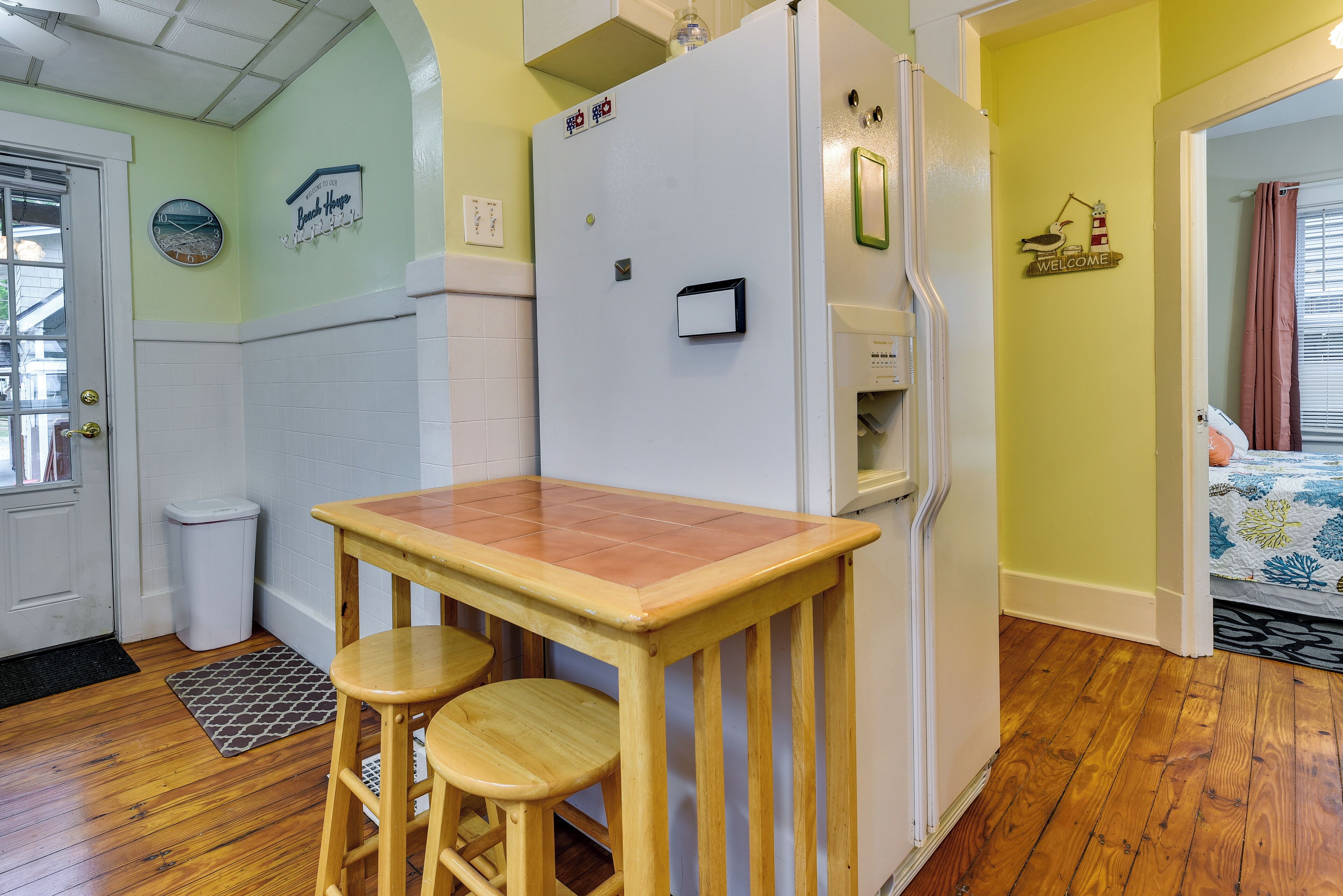 A compact kitchen with a refrigerator, a sink, and a wooden table with two stools.