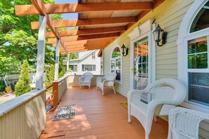 A covered porch with white wicker chairs, a wooden railing, and a view of neighboring houses. - Turtle Cove Bay Beach House ~ 13 Mi to Buffalo! (Lake View)