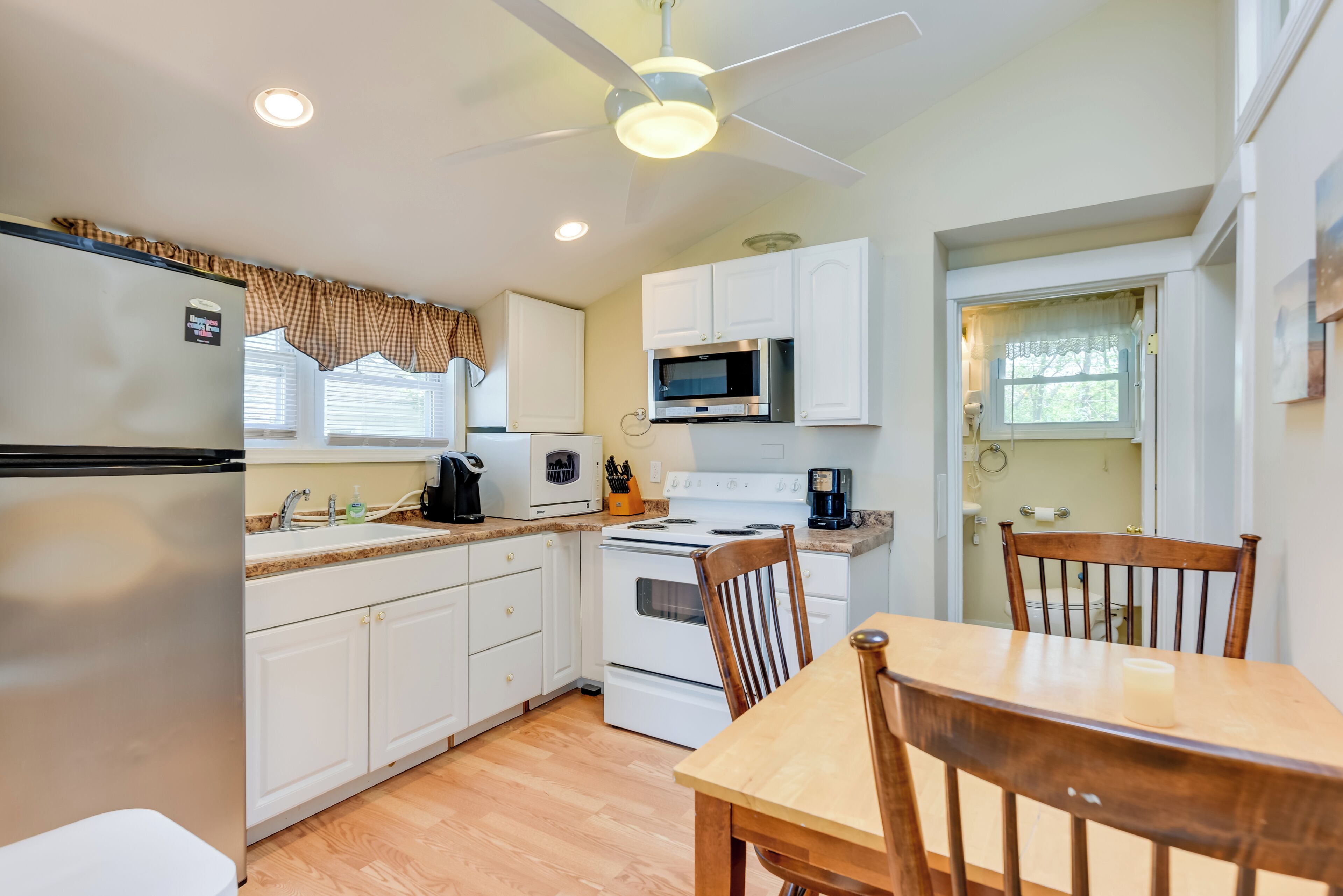 A compact kitchen with white cabinets, a microwave, stove, and a ceiling fan.