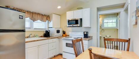 A compact kitchen with white cabinets, a microwave, stove, and a ceiling fan.