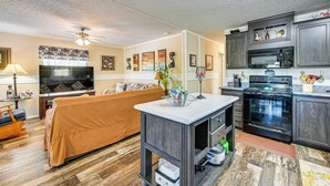 Una sala de estar moderna con sofá, televisión y área de cocina que incluye microondas y horno.