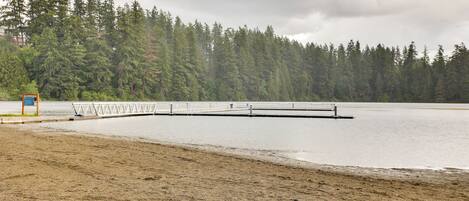 A sandy beach with a wooden pier extending into a calm lake, surrounded by dense forest.