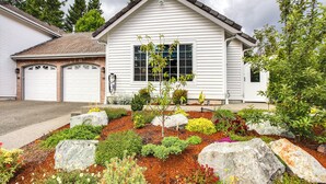 Ein zweistöckiges Haus mit Garage, ein gepflegter Garten mit verschiedenen Pflanzen und Steinen sowie freie Sicht zum Himmel.