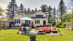Une maison à deux étages dotée d’un patio aménagé avec des meubles d’extérieur, un foyer et un espace salon couvert.
