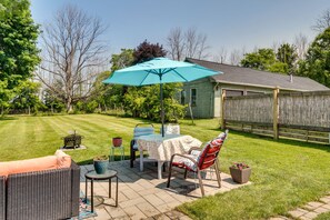A patio with a table and chairs, a blue umbrella, and a house in the background. - Walworth Home w/ Hot Tub - Near Golf Courses! (Walworth)