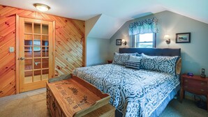 Ein Schlafzimmer mit Holztür, einem Bett mit gemusterten Betttextilien, einem Nachttisch mit Lampe und einem Beistelltisch mit Telefon.